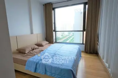 Spacious bedroom with large window offering city view and natural light.
