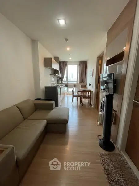 Modern open-layout living room with kitchen and dining area, featuring sleek furniture and natural light.