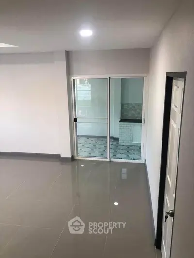 Spacious modern living room with sleek tile flooring and sliding glass doors leading to a stylish kitchen.