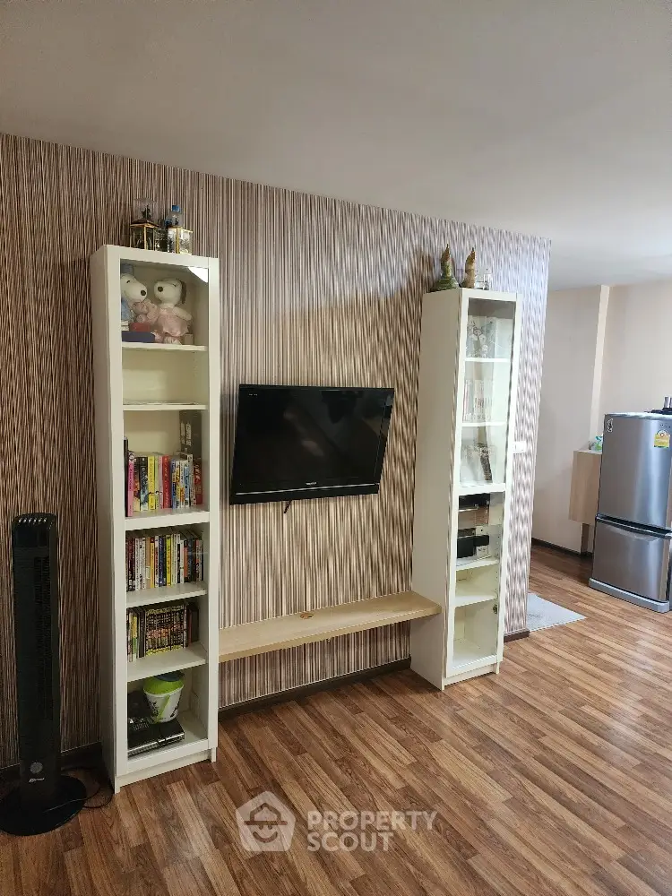 Spacious living room with modern wood flooring, stylish wallpaper, and built-in shelving units flanking a sleek flat-screen TV.
