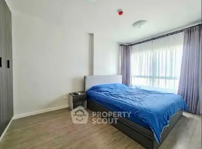 Spacious bedroom with large window and modern furnishings in a bright apartment.