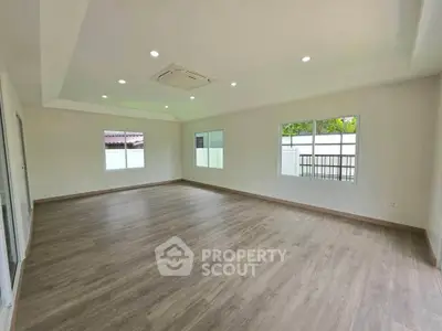 Spacious empty room with wooden flooring and large windows, perfect for customization.