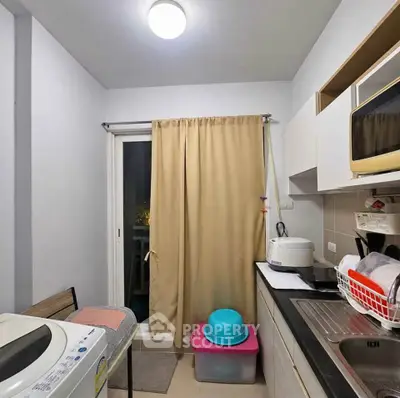 Compact kitchen with washing machine and microwave in modern apartment
