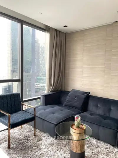Modern living room with plush sofa, glass table, and city view through large windows.