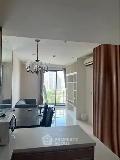 Modern living room with city view, elegant chandelier, and sleek shelving in a high-rise apartment.