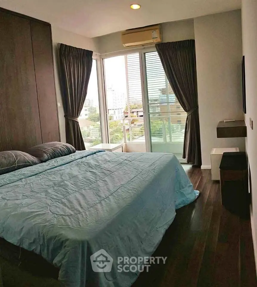 Modern bedroom with large windows and city view, featuring elegant dark curtains and wooden flooring.