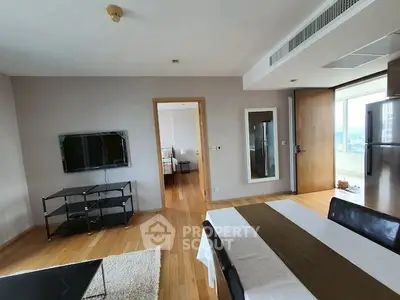 Modern living room with dining area and view into bedroom, featuring hardwood floors and wall-mounted TV.