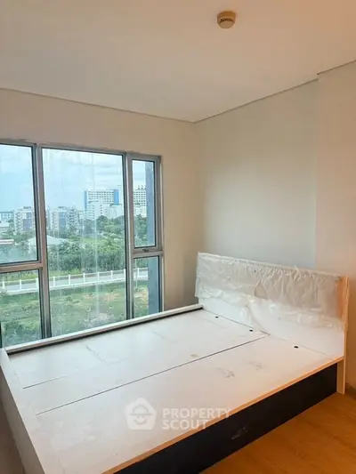 Bright bedroom with large windows offering a stunning city view, featuring a modern bed frame and wooden flooring.