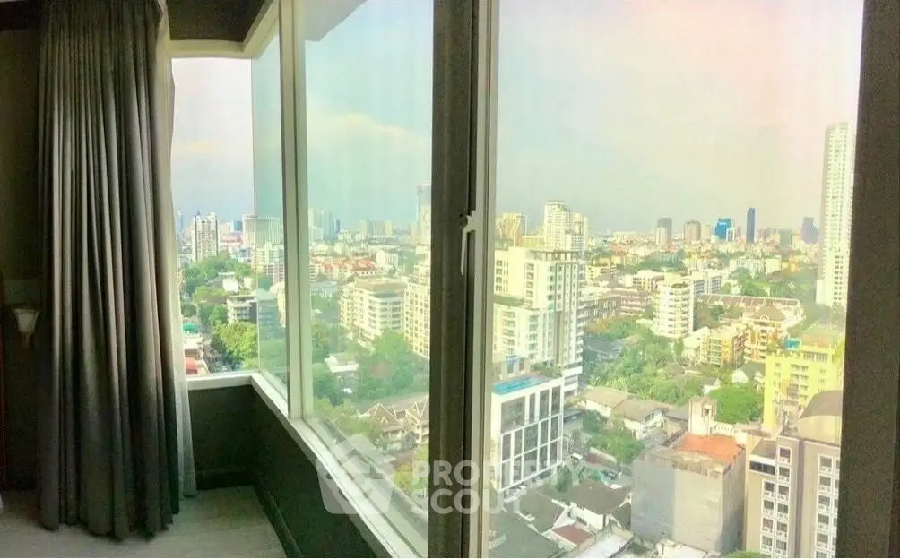 Stunning cityscape view from a high-rise apartment window, showcasing urban skyline and lush greenery.