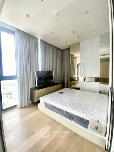 Modern bedroom with large window and sleek furnishings in a high-rise apartment.