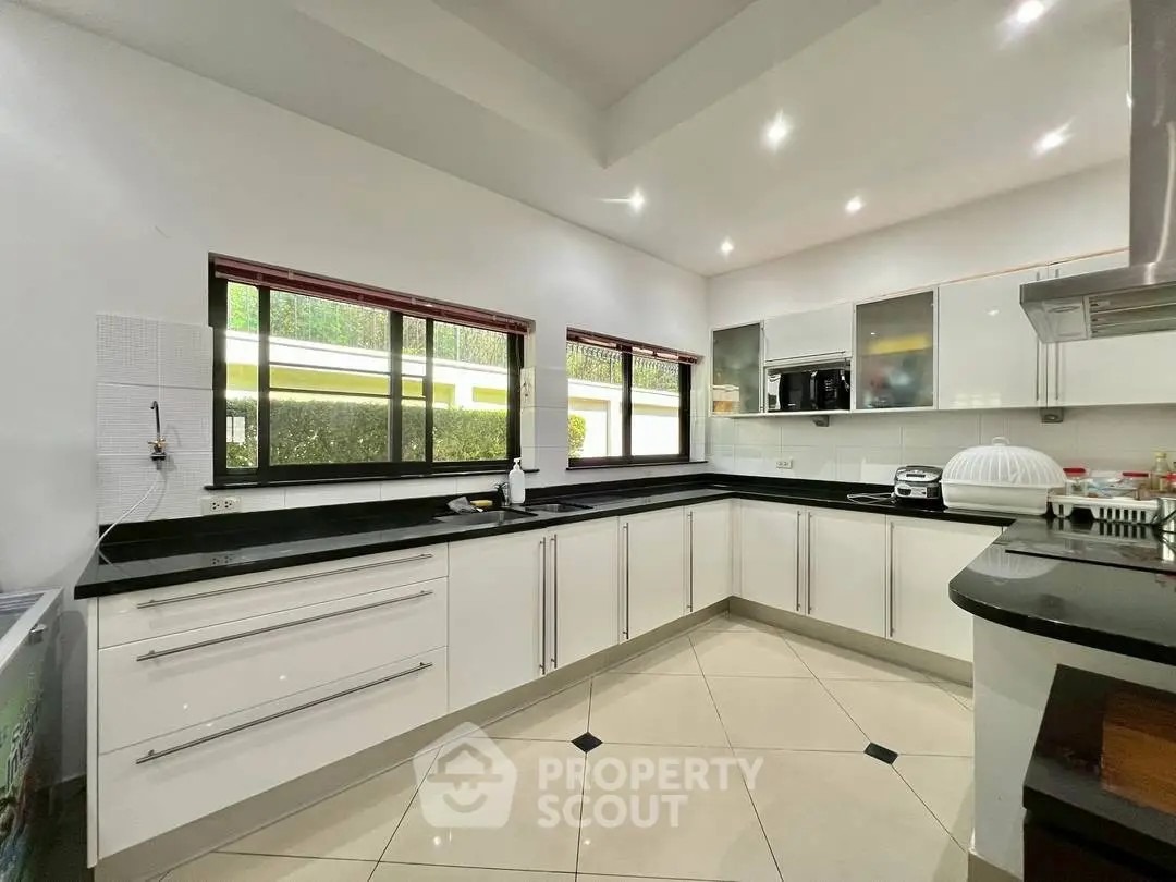 Spacious modern kitchen with sleek white cabinets and black countertops, featuring large windows for natural light.
