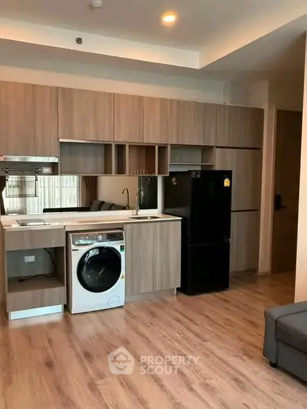 Modern kitchen with sleek cabinetry, washing machine, and fridge in stylish apartment.