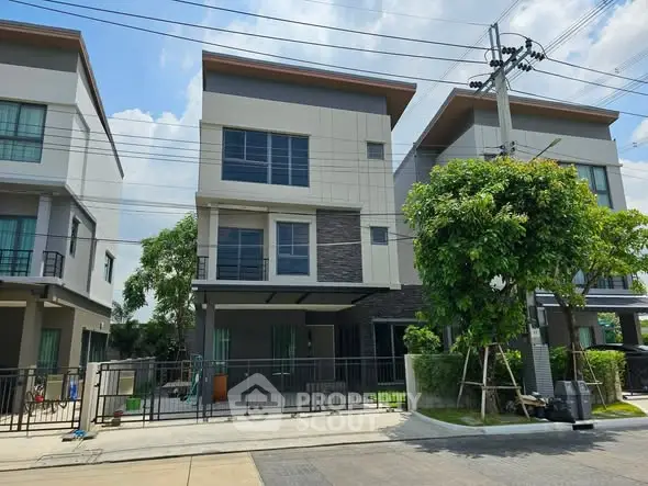 Modern three-story townhouse with sleek design and lush greenery in a suburban neighborhood.
