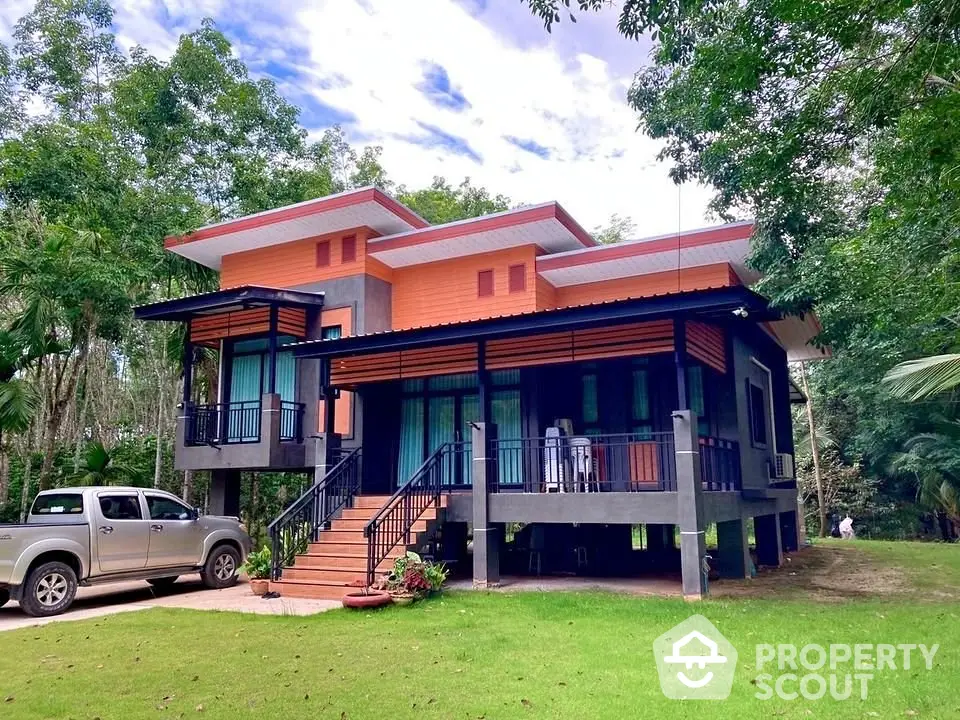 Modern two-story house with unique architectural design surrounded by lush greenery and parked vehicle.