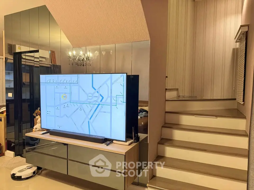 Modern living room with sleek TV unit and elegant staircase, featuring contemporary decor and ambient lighting.