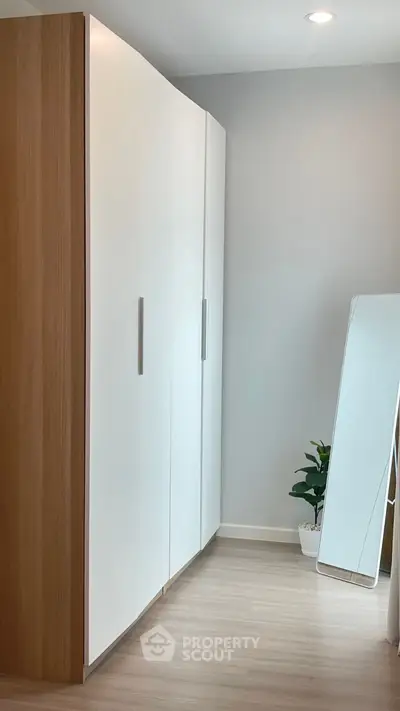 Modern storage space with sleek white wardrobe and full-length mirror in a stylish room.