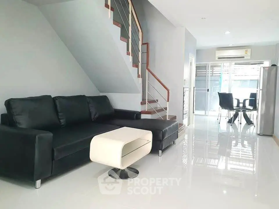 Modern living room with sleek black sofa and stylish staircase in open layout home.