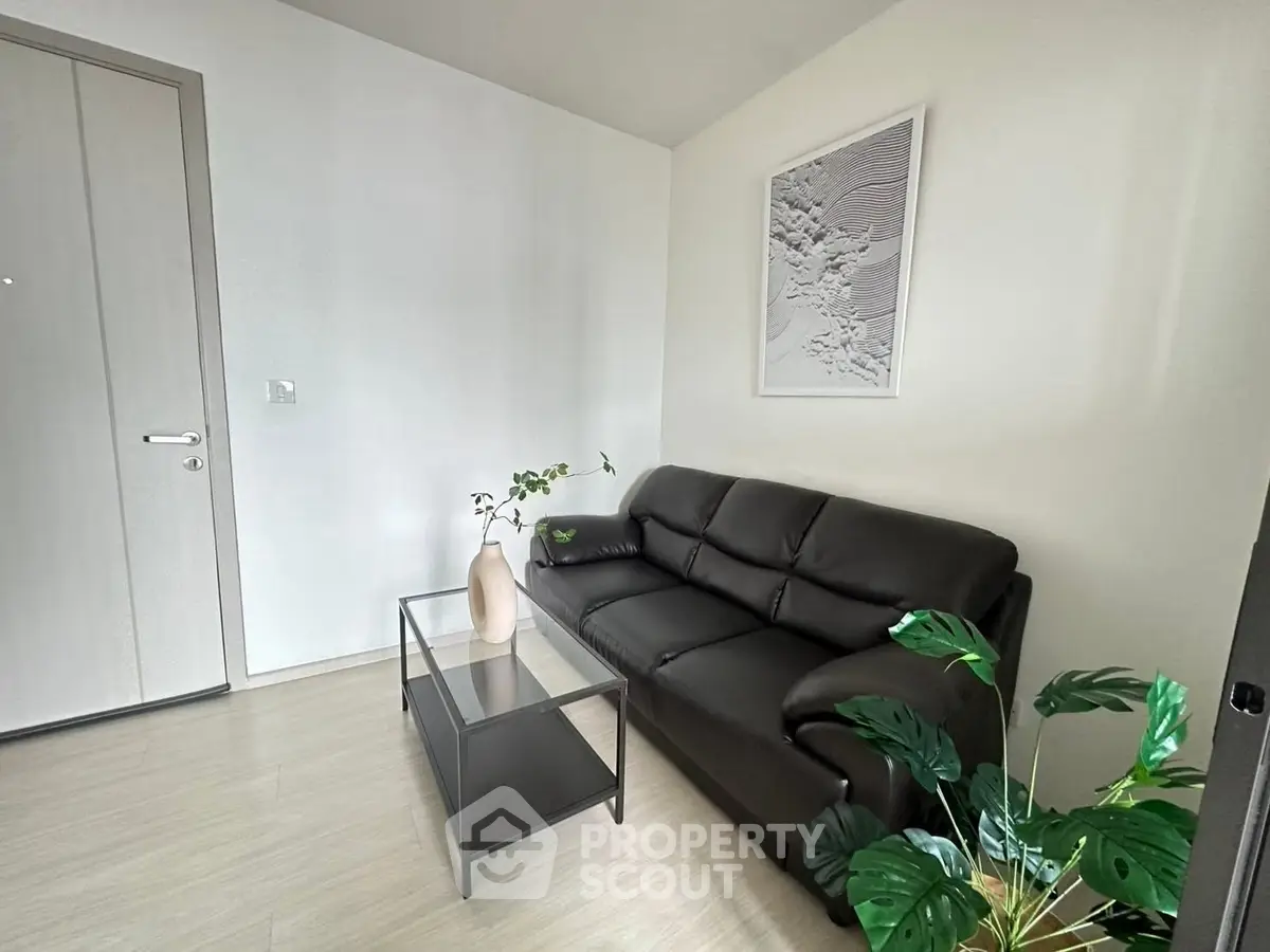 Modern living room with sleek black leather sofa and glass coffee table, accented by lush green plants.