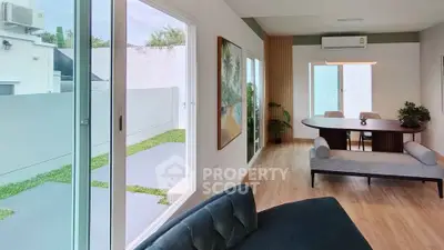 Modern living room with large windows and garden view, featuring stylish furniture and wooden flooring.