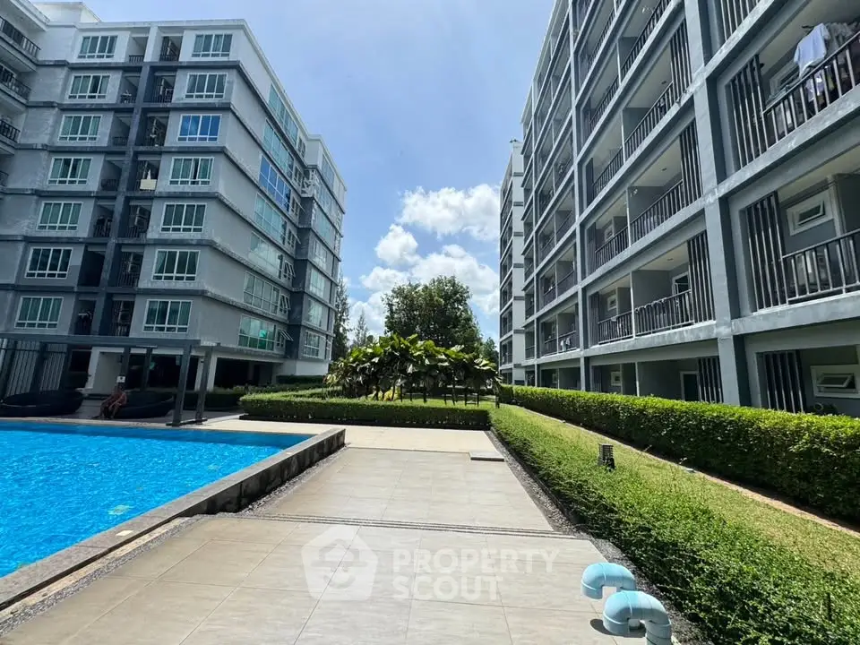 Modern apartment complex with pool and lush greenery under a bright blue sky.