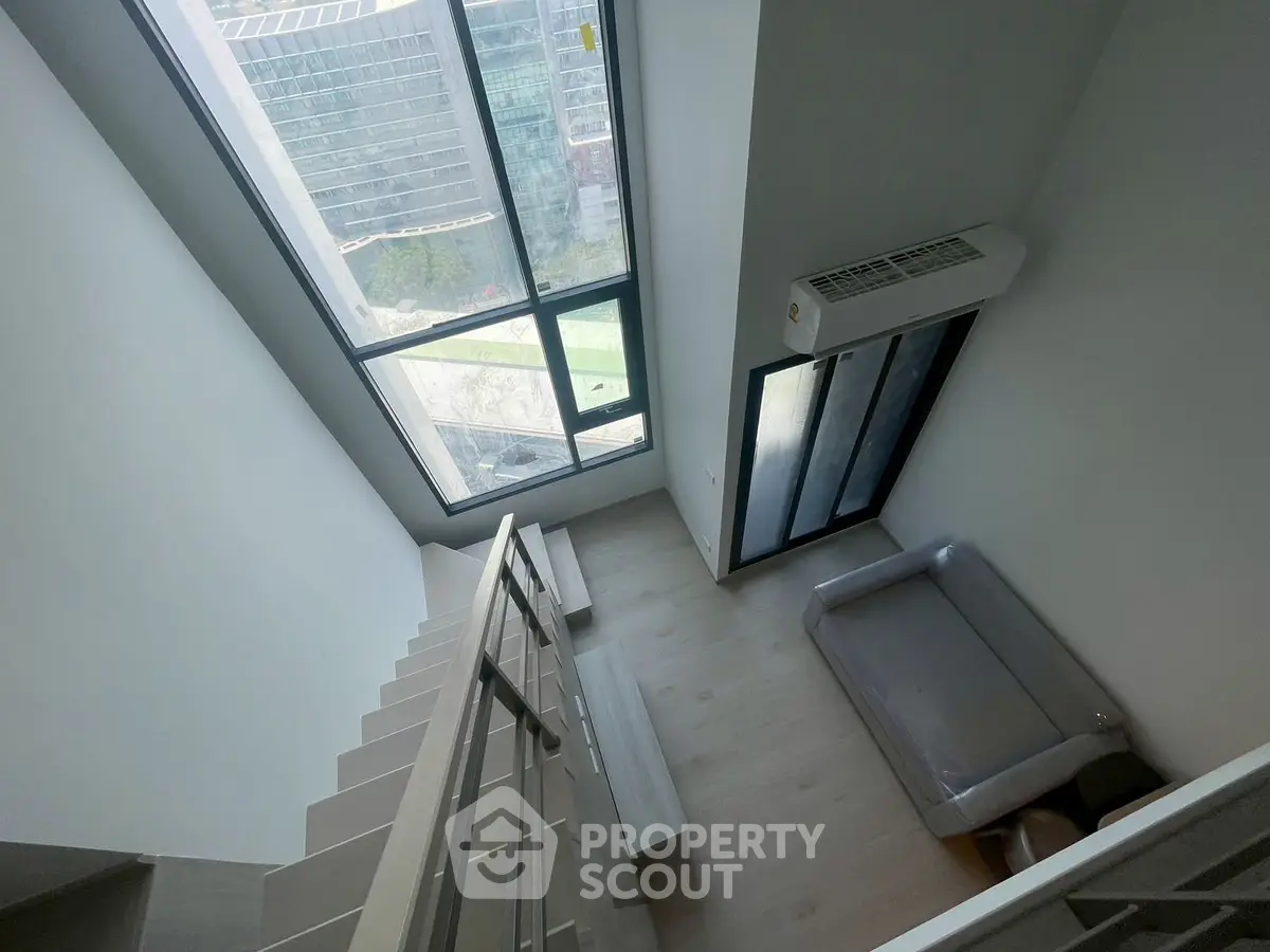 Modern loft apartment with large windows and city view, featuring a sleek staircase and minimalist design.