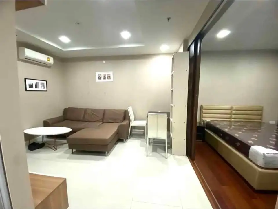 Modern living room with cozy sofa and adjacent bedroom in open layout apartment.