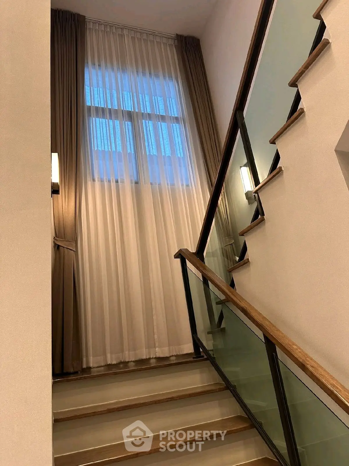 Elegant staircase with modern glass railing and tall window with curtains