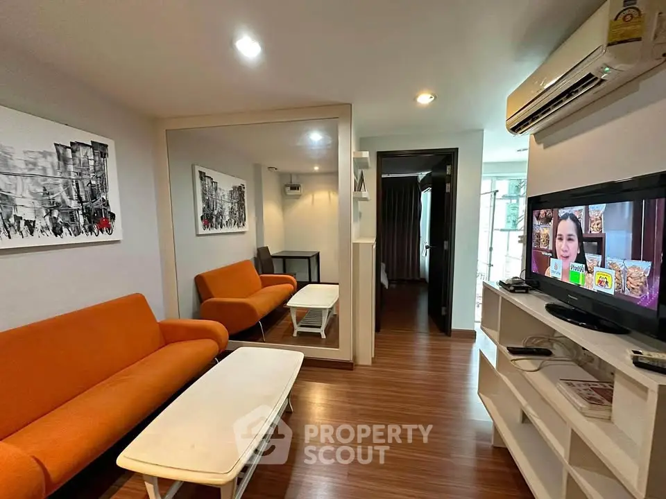 Modern living room with orange sofas, wall art, and a TV in a cozy apartment.