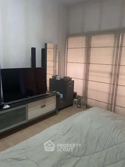 Cozy bedroom with modern TV setup and ample natural light from large windows.