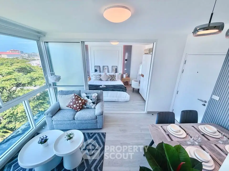 Modern open-plan living room with dining area and bedroom, featuring large windows and stylish decor.