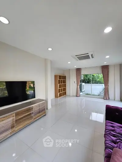 Spacious living room with modern decor and large windows offering natural light and garden view.