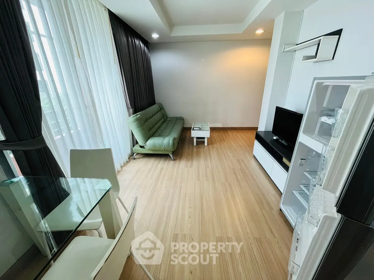 Modern living room with sleek furniture and natural light, featuring a green sofa and flat-screen TV.