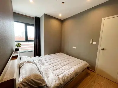 Modern bedroom with cozy bedding and large window offering city views.