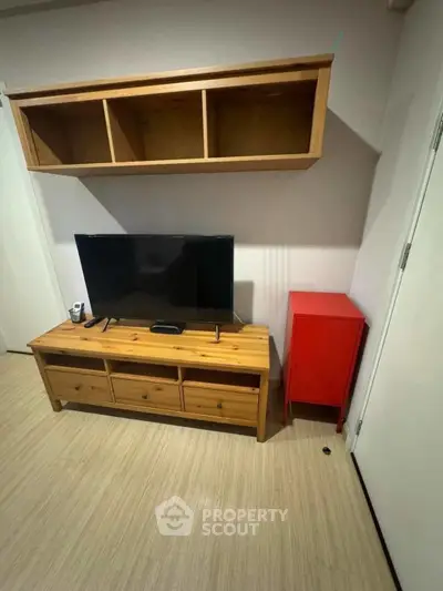 Cozy living room with wooden TV stand and wall-mounted shelf, featuring a modern flat-screen TV.