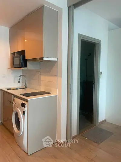 Modern compact kitchen with washing machine and sleek cabinetry in a cozy apartment.