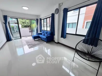 Spacious living room with modern blue sofa and large windows offering natural light and garden view.