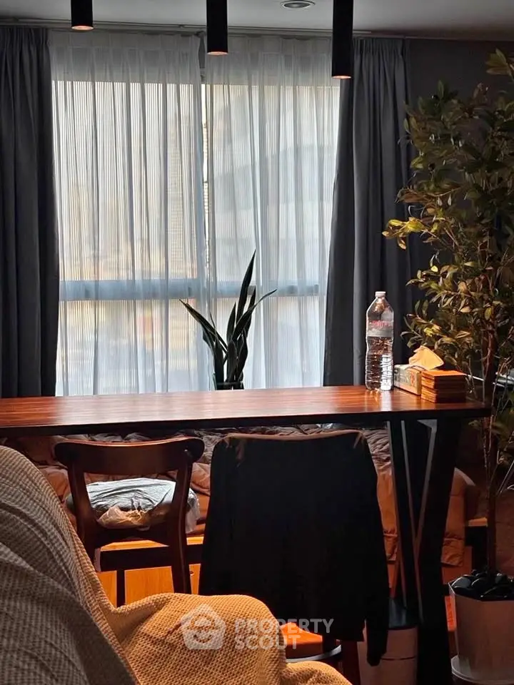 Cozy living room with elegant wooden table, chairs, and lush indoor plants, bathed in warm natural light.