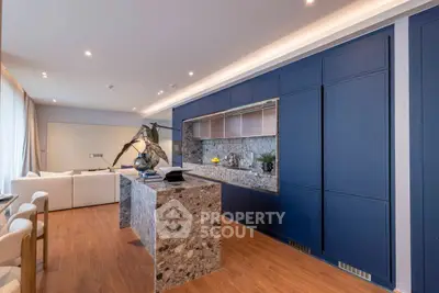 Luxurious modern kitchen with sleek blue cabinetry and elegant stone island in open-plan living space.