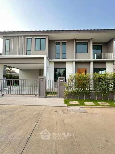 Modern two-story house with sleek design and gated entrance, featuring large windows and a small garden.
