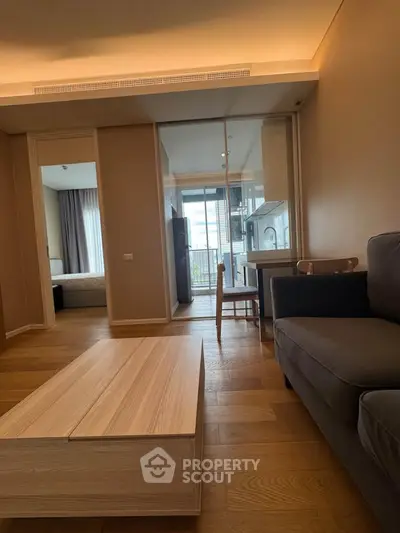 Modern living room with wooden flooring and glass partition leading to a cozy bedroom and balcony view.