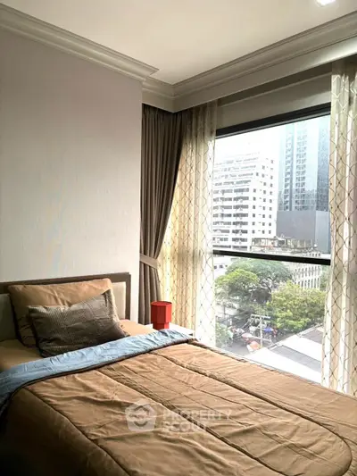 Cozy bedroom with city view, featuring large window and elegant curtains, perfect for urban living.