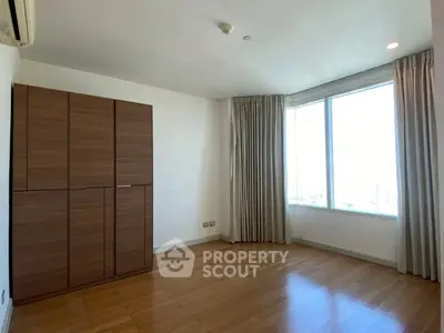 Spacious bedroom with wooden flooring and large window offering natural light.