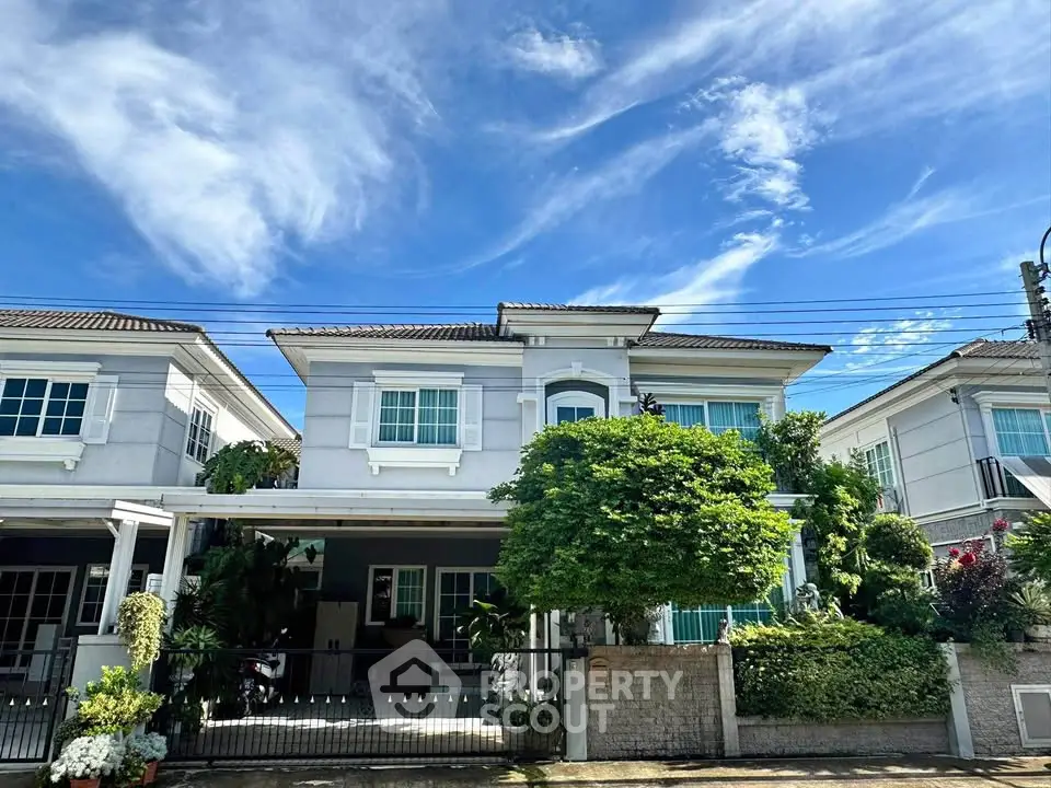 Charming two-story house with lush garden and clear blue sky backdrop.
