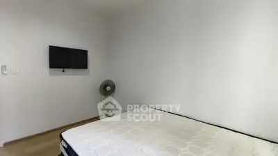Minimalist bedroom with wall-mounted TV and fan, featuring a comfortable mattress and wooden flooring.