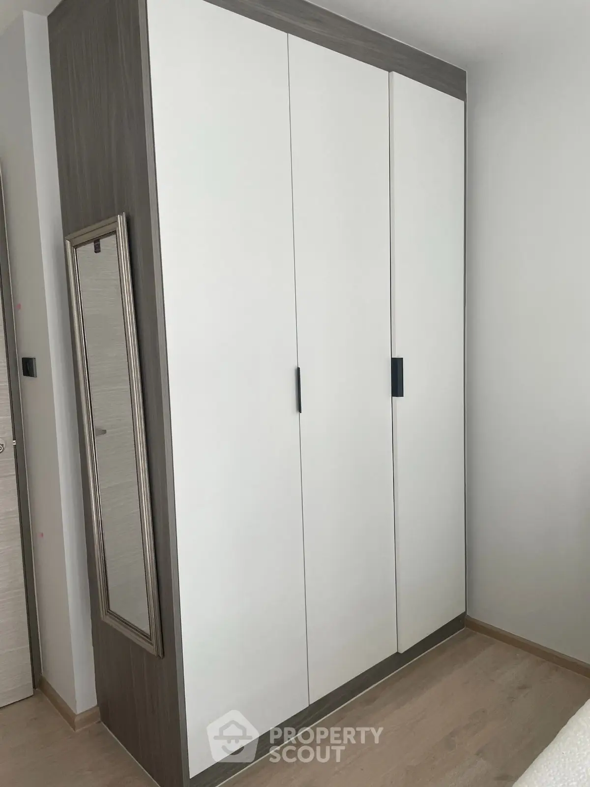 Modern bedroom with sleek wardrobe and full-length mirror, showcasing minimalist design and ample storage space.