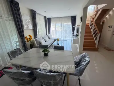 Modern living room with dining area and staircase, featuring elegant decor and natural light.