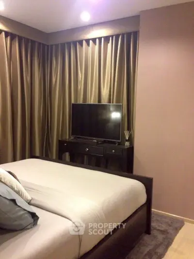Cozy bedroom with elegant curtains and modern TV setup, perfect for relaxation.