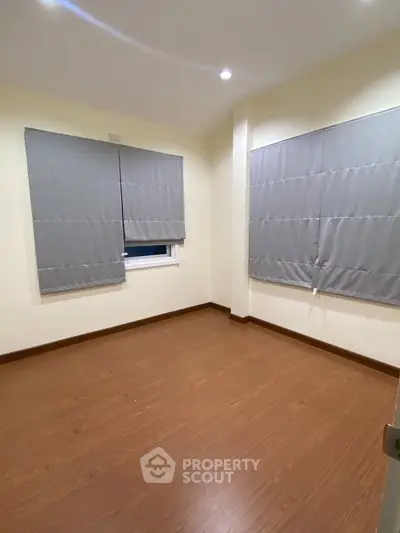 Spacious empty room with wooden flooring and large windows, perfect for customization.