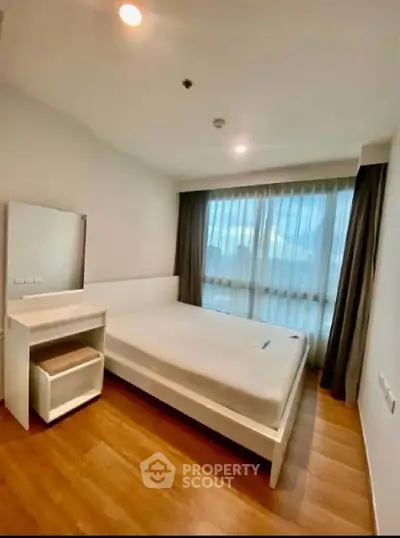 Modern bedroom with large window and wooden flooring in a stylish apartment.