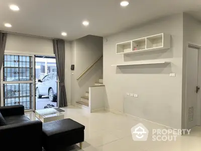 Modern living room with sleek design and staircase, featuring black sofa and large window for natural light.